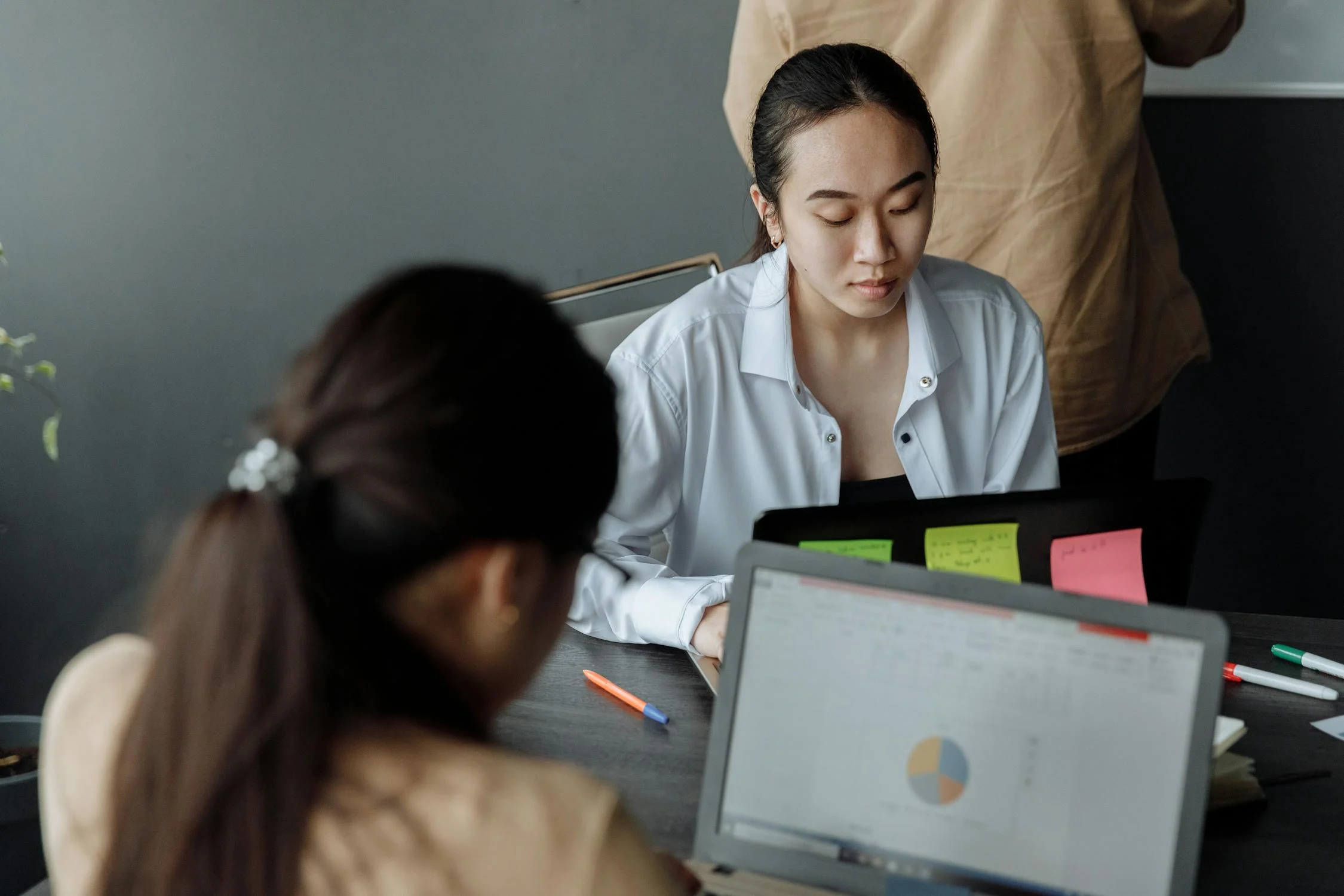 two employees working with their laptop in the office to track business expenses with pie chart